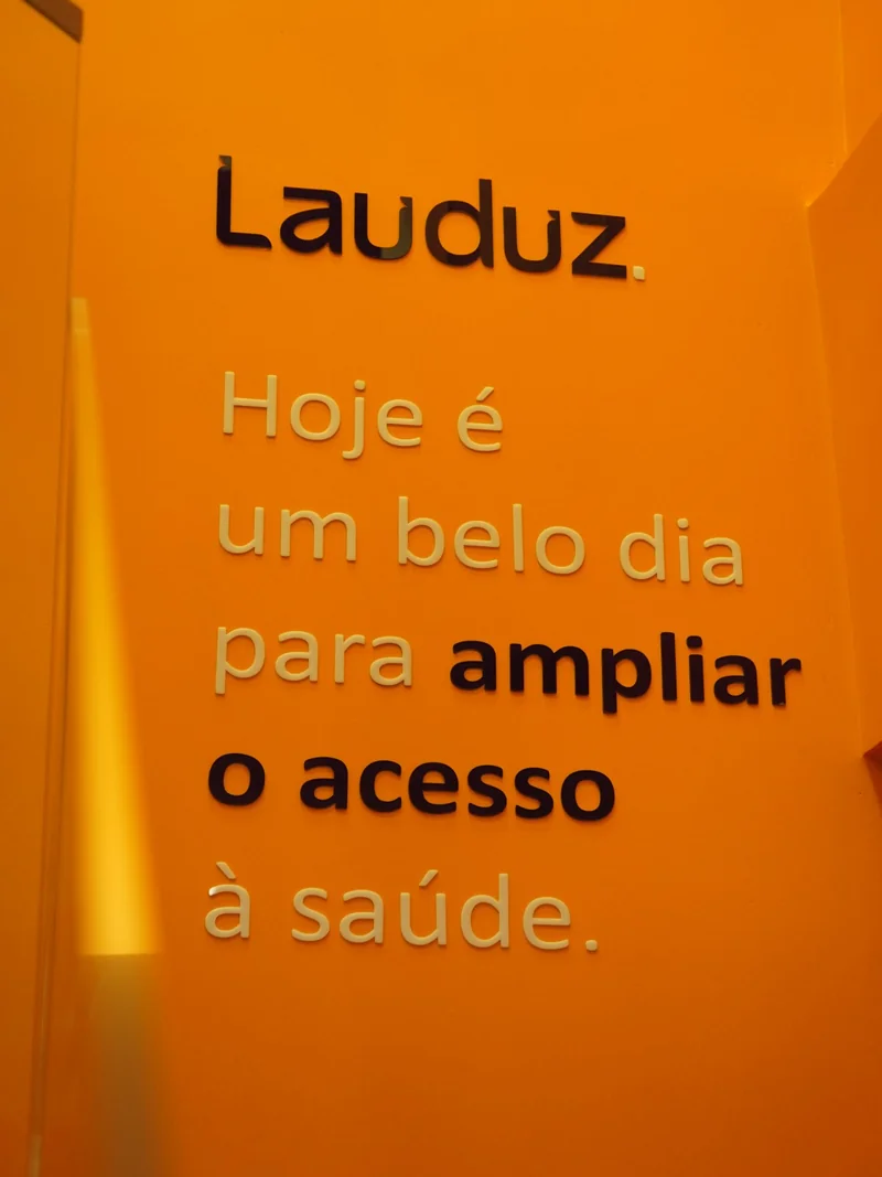 Parede-manifesto da nova sede da Lauduz, em laranja, com a frase 'Hoje é um belo dia para ampliar o acesso à saúde'