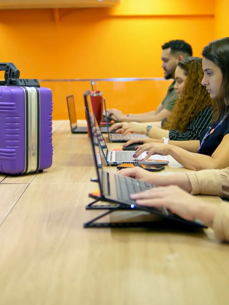 Equipe da Lauduz trabalhando na bancada da nova sede em Vila Velha, com um Telekit® sobre a mesa e a parede laranja ao fundo